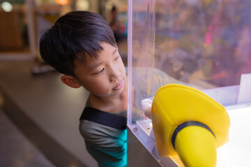Asian boy at one of the mall stores, playing Claw Game. - obrazy, fototapety, plakaty