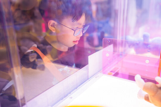 Asian boy at one of the mall stores, playing Claw Game.