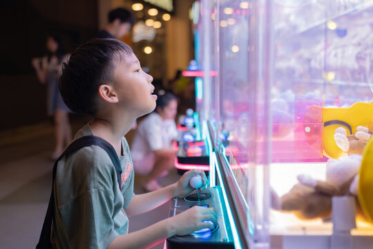 Asian boy at one of the mall stores, playing Claw Game.