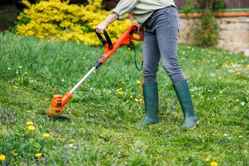 Fotobehang Olijf Woman gardener using electric weed trimmer to trim grass in garden. Lawn care in yard  © encierro