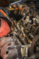 The mechanic is repairing a car engine. He is holding pliers in his hand. Cylinder head. Valve. Sixteen valves. Valve springs. Engine block. Car repairing. Auto service.