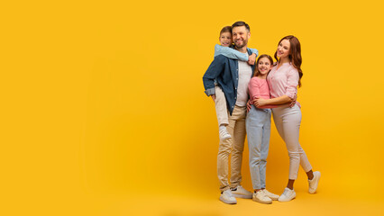 Family embraced and smiling on yellow background
