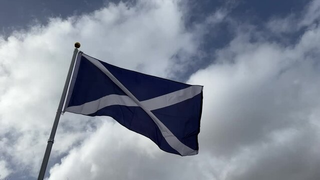 Slow motion of Scotland flag (the Saltire), filmed on a sunny day with blue sky and white clouds.