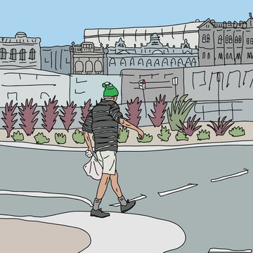 Man with green beanie and bag walking across street with historic buildings in background
