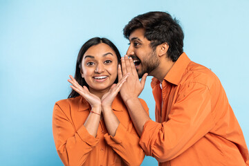 Excited couple sharing secret on blue background