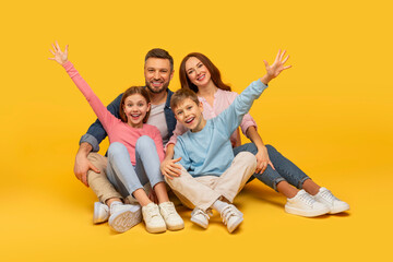 Family spreading arms wide with joy on yellow