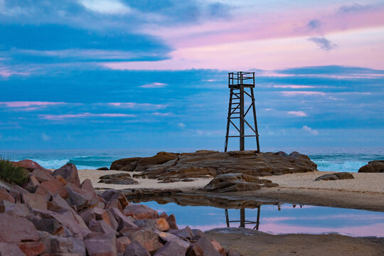 Old wooden lifeguard, shark lookout tower on Redhead Beach with reflection