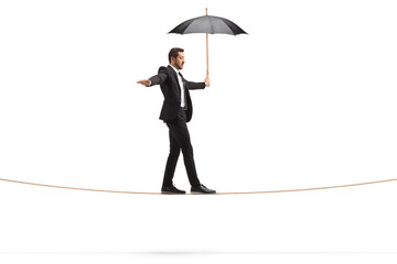 Full length profile shot of a businessman with an umbrella walking on a rope
