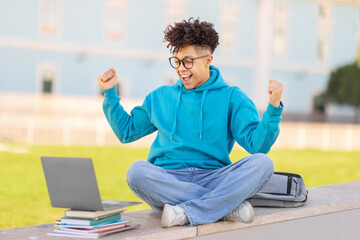 Student celebrating success with raised fists, studying at park