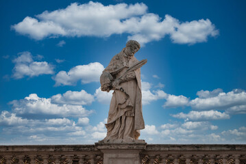 Obraz premium Stone statue of religious figure holding book and key against blue sky in Vatican. Weathered, with decorative balustrade. Rich collection of Vatican art.