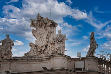 Fototapeta na wymiar Ornate architectural details in Vatican City rooftop statues, coat of arms, religious figures in contemplative pose. Dramatic sky with historical significance and modern elements.