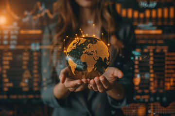 Fototapeta premium Close-up of a businesswoman's hands holding a glowing globe, symbolizing global business strategies and sustainability, with charts and graphs projected in the background.