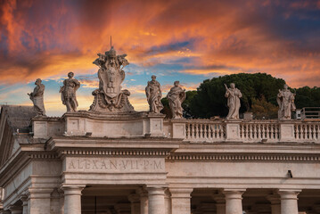 Stunning view of classical statues and architecture in Vatican. Statues on balustrade, central sculpture with papal symbols, building facade with inscriptions and dramatic sunset sky.uul - obrazy, fototapety, plakaty