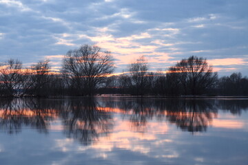 Reflection of the sunset, clouds and tree crowns in the water mirror when the Staritsa River floods