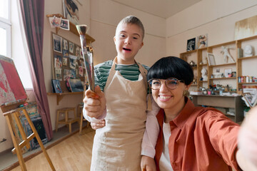 POV of smiling art teacher taking selfie photo with young student in studio and looking at camera...