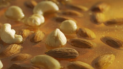 Healthy organic honey. Sweet fresh golden honey on the yellow background, almonds walnuts and cashew nuts in the thick syrup, close up shot.