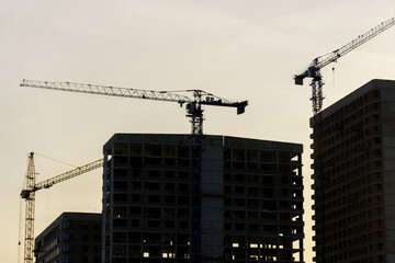 Construction cranes on top of a building under construction. The cranes are engaged in the construction work of the building.