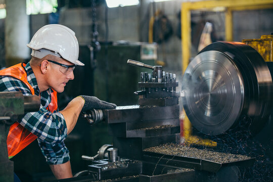 Male engineer metalworker industrial experienced operator technician worker in safety hard helmet working on lathe machine, professional man in industry technology manufacturing factory workshop