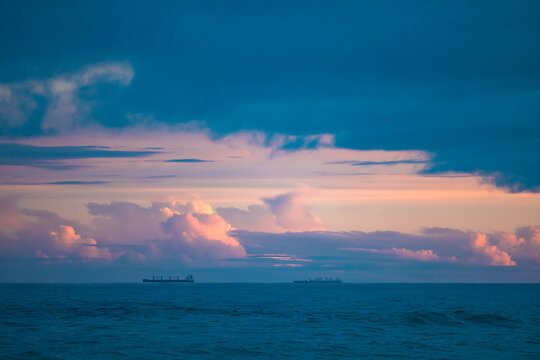 Cargo ships lined up at sea on their way to Newcastle Harbour under a vibrant sunset sky