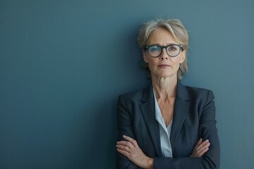A woman wearing glasses and a suit stands with her arms crossed