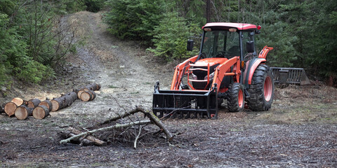 Orange tractor in front of a pacific northwest woodland trail near logs.