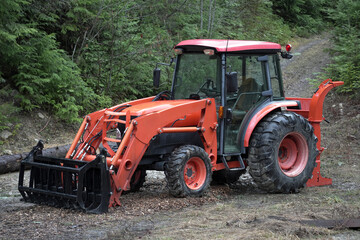Orange tractor in front of a pacific northwest woodland trail near logs.