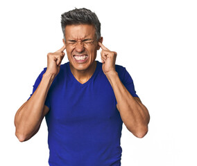 Middle-aged Latino man covering ears with hands.