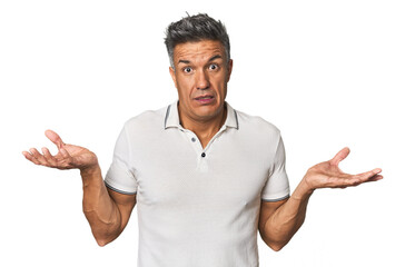 Middle-aged Latino man doubting and shrugging shoulders in questioning gesture.
