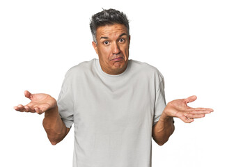 Middle-aged Latino man doubting and shrugging shoulders in questioning gesture.