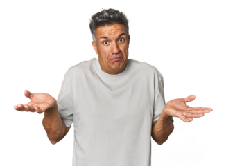 Middle-aged Latino man doubting and shrugging shoulders in questioning gesture.