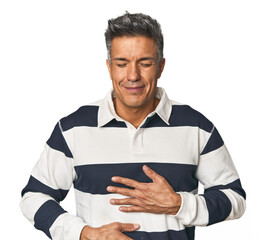 Middle-aged Latino man laughs happily and has fun keeping hands on stomach.