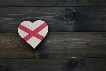wooden heart with national flag of alabama state on the wooden background.