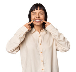 Young Hispanic woman with short black hair in studio smiles, pointing fingers at mouth.