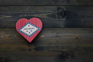 wooden heart with national flag of arkansas state on the wooden background.