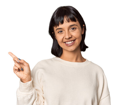 Young Hispanic woman with short black hair in studio smiling cheerfully pointing with forefinger away.