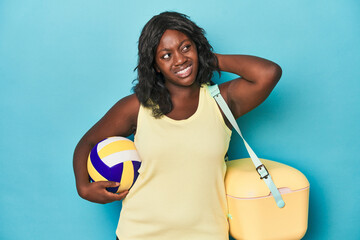 Young curvy woman with cooler and ball touching back of head, thinking and making a choice.