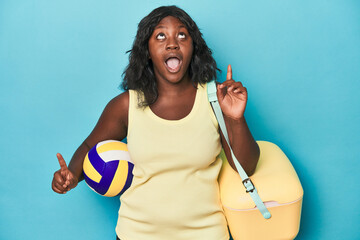Young curvy woman with cooler and ball pointing upside with opened mouth.