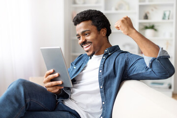 Joyful Black Man Celebrating Victory With Digital Tablet at Home