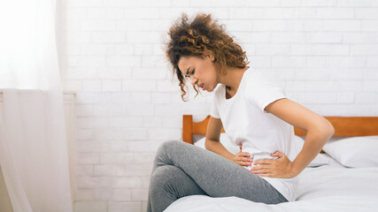 Unhappy woman suffering from stomachache, sitting on bed