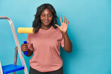 Curvy woman with paint roller and ladder smiling cheerful showing number five with fingers.