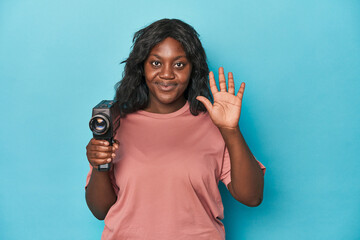 Curvy lady with vintage film camera smiling cheerful showing number five with fingers.