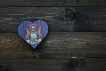 wooden heart with national flag of michigan state on the wooden background.