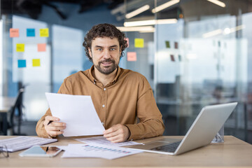 Confident mature hispanic businessman with a friendly smile reviewing documents in a modern office setting.