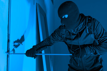 Masked burglar prying window open with crowbar