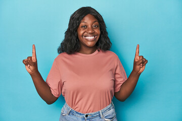 Young african american curvy woman indicates with both fore fingers up showing a blank space.