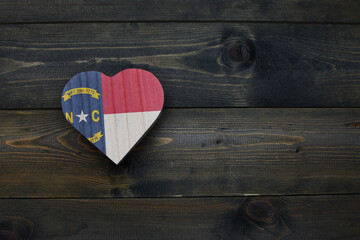 wooden heart with national flag of north carolina state on the wooden background.