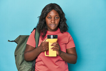 Ready for adventure, curvy woman with backpack on blue backdrop - obrazy, fototapety, plakaty