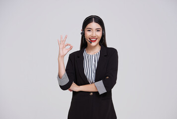 Happy young asian business woman call centre showing OK sign. Welcome female operator put on smalltalk headphone standing isolated on white background.