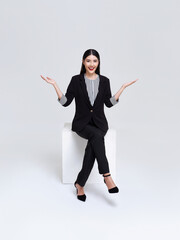 Attractive beautiful Asian woman sitting on white chair and hands up raised arms from happiness, businesswoman presenting or showing open hand palm for product