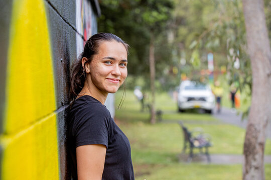 Aboriginal woman leaning against an urban park wall smiling at the camera